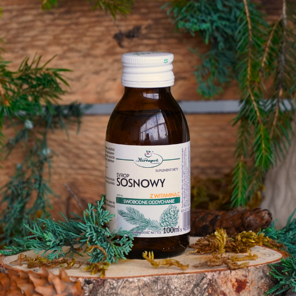 Bottle of 'Sosnowy' syrup with a label on a wooden surface with pine branches.